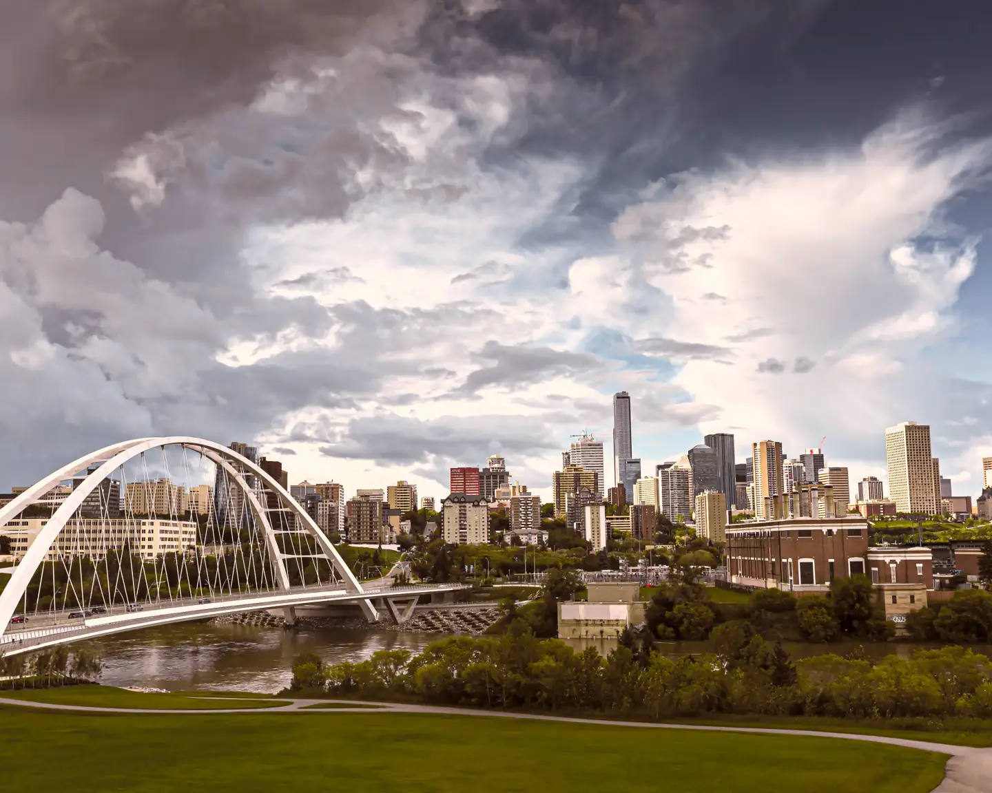 Panoramic view of the skyline of Edmonton, Canada, with a modern bridge over the North Saskatchewan River and sky in the background.
