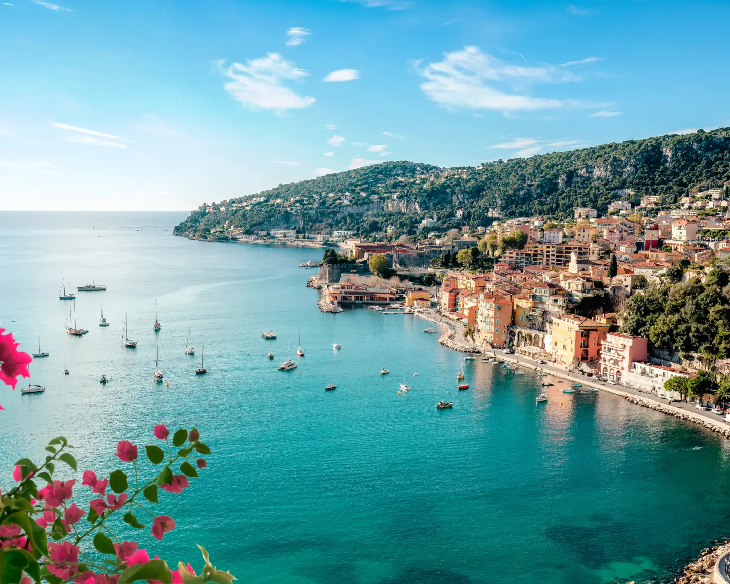 View of the coast of Nice, France, with turquoise water, boats and colorful houses beneath a blue sky.