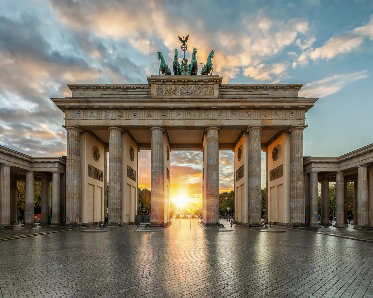 The Brandenburg Gate in Berlin at sunrise, with the sun shining through the columns and lighting up the sky in warm hues.