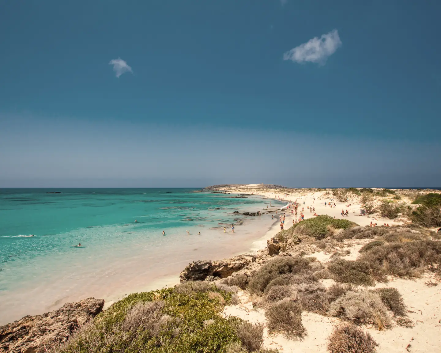 Het prachtige strand van Elafonissi in Chania met kristalhelder turquoise wateren, zandduinen en schaarse vegetatie langs de kust onder een stralend blauwe lucht.