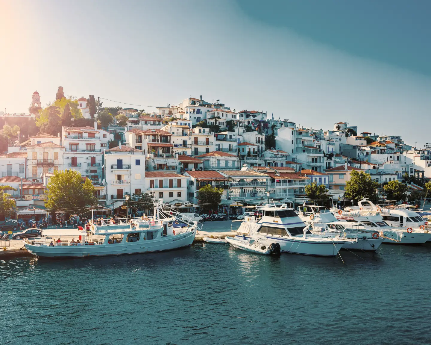 Die Stadt Skiathos mit vielen Gebäuden am Berg sowie einigen Booten direkt am Anleger im Wasser in Griechenland am Nachmittag.