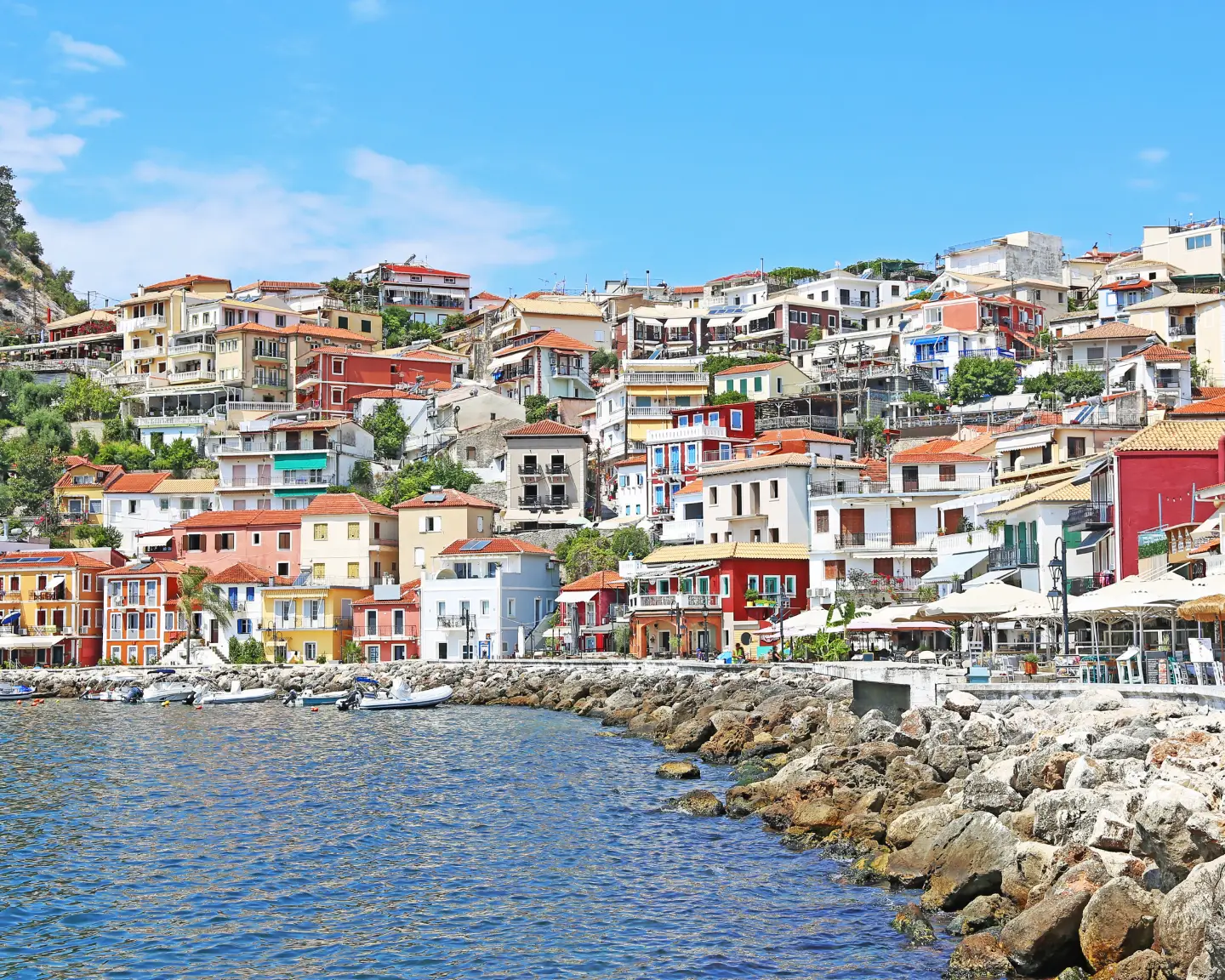 Blick auf die Stadt Parga in Griechenland, mit bunten Häusern entlang der Küste und einer Promenade.