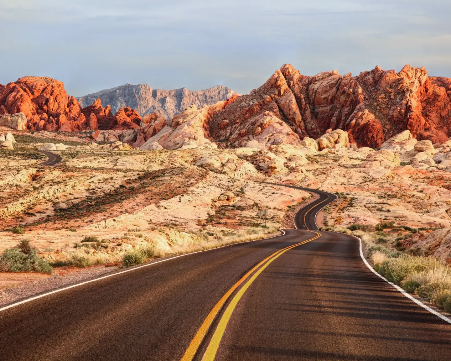 Een weg in het Valley of Fire State Park met rode rotsformaties en een woestijnlandschap aan de horizon